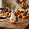 A ceramic goose figurine wearing a patterned outfit and headband, displayed on a wooden table with autumn decor.
