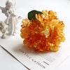 A bouquet of orange silk hydrangea stems with vintage burnt edge petals next to a white figurine.