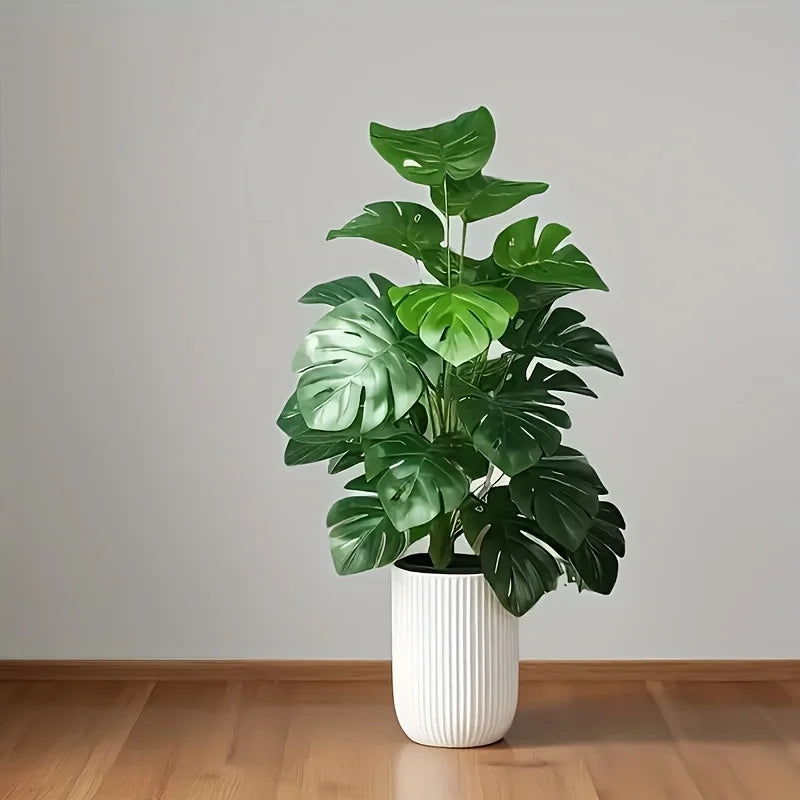 A vibrant green artificial monstera palm plant in a white cylindrical pot displayed on a wooden floor.