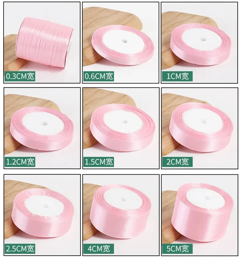 A collection of pink silk satin ribbons in various widths, ranging from 0.3cm to 5cm, displayed on a wooden surface.