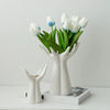 White ceramic hand vase holding a bouquet of blue and white tulips