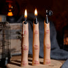Three tall candles with black wax and lit flames stand on a woven mat in a dark setting.