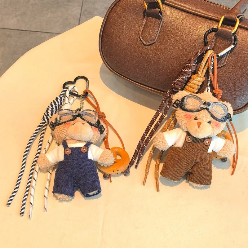 Un ours en peluche en porte-clés portant des lunettes aviateur et une combinaison avec des sangles en cuir sur une surface cl