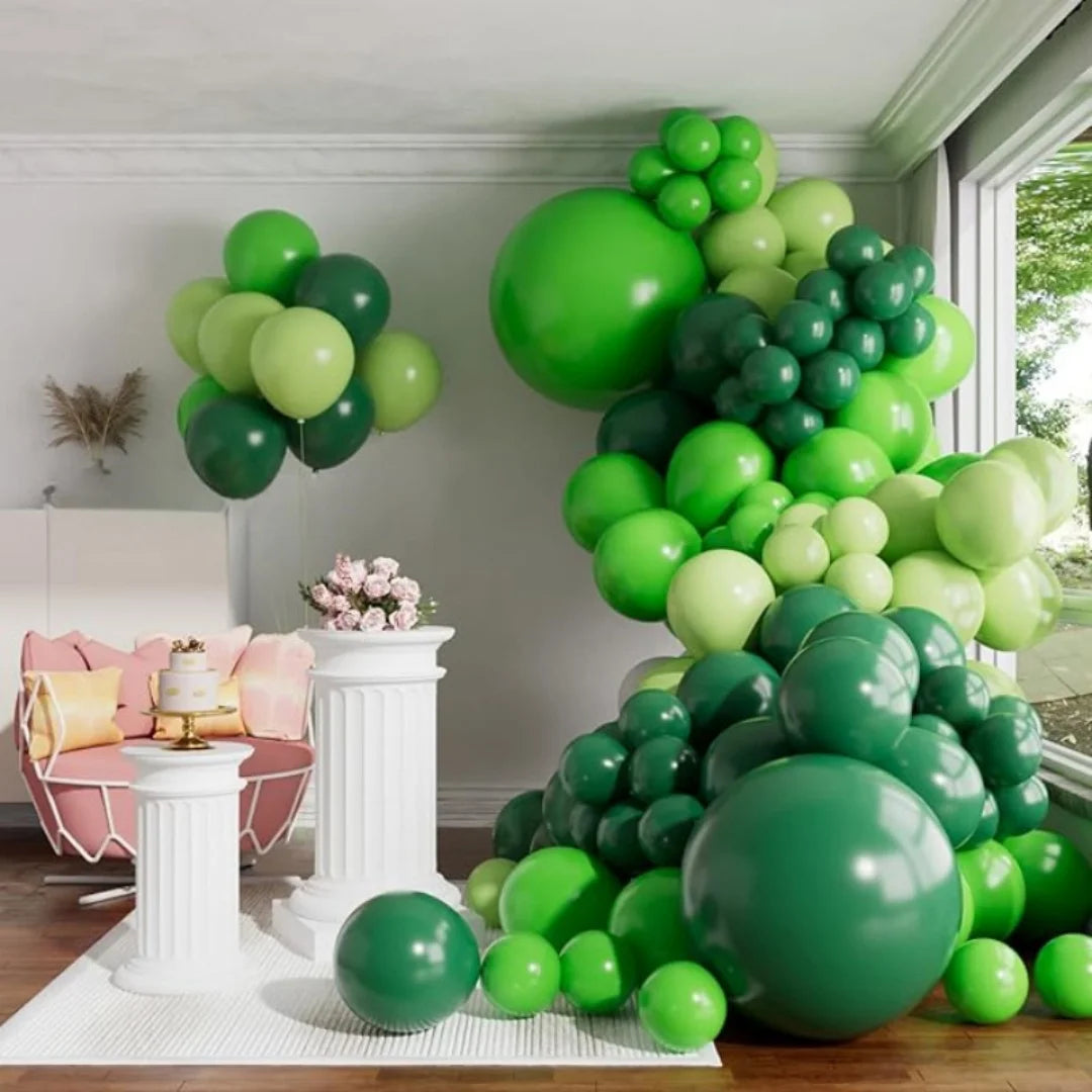 A large green balloon garland arch display featuring various shades of green balloons in a white room.