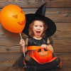 A young girl wearing a black witch hat and holding an orange pumpkin balloon with a carved face.