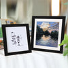 Two black photo frames display calligraphy and a landscape painting on a white surface.