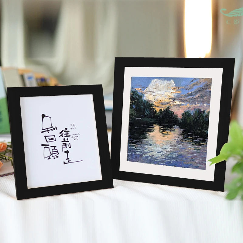 Two black photo frames display calligraphy and a landscape painting on a white surface.