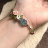 A handmade macrame bracelet featuring rose accents and a blue aquamarine stone on a person's wrist.