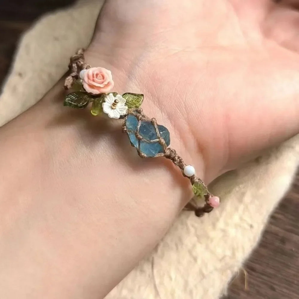 A handmade macrame bracelet featuring rose accents and a blue aquamarine stone on a person's wrist.