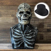 Sculpture de masque crâne réaliste avec détails faciaux et chapeau haut en noir sur fond en bois.