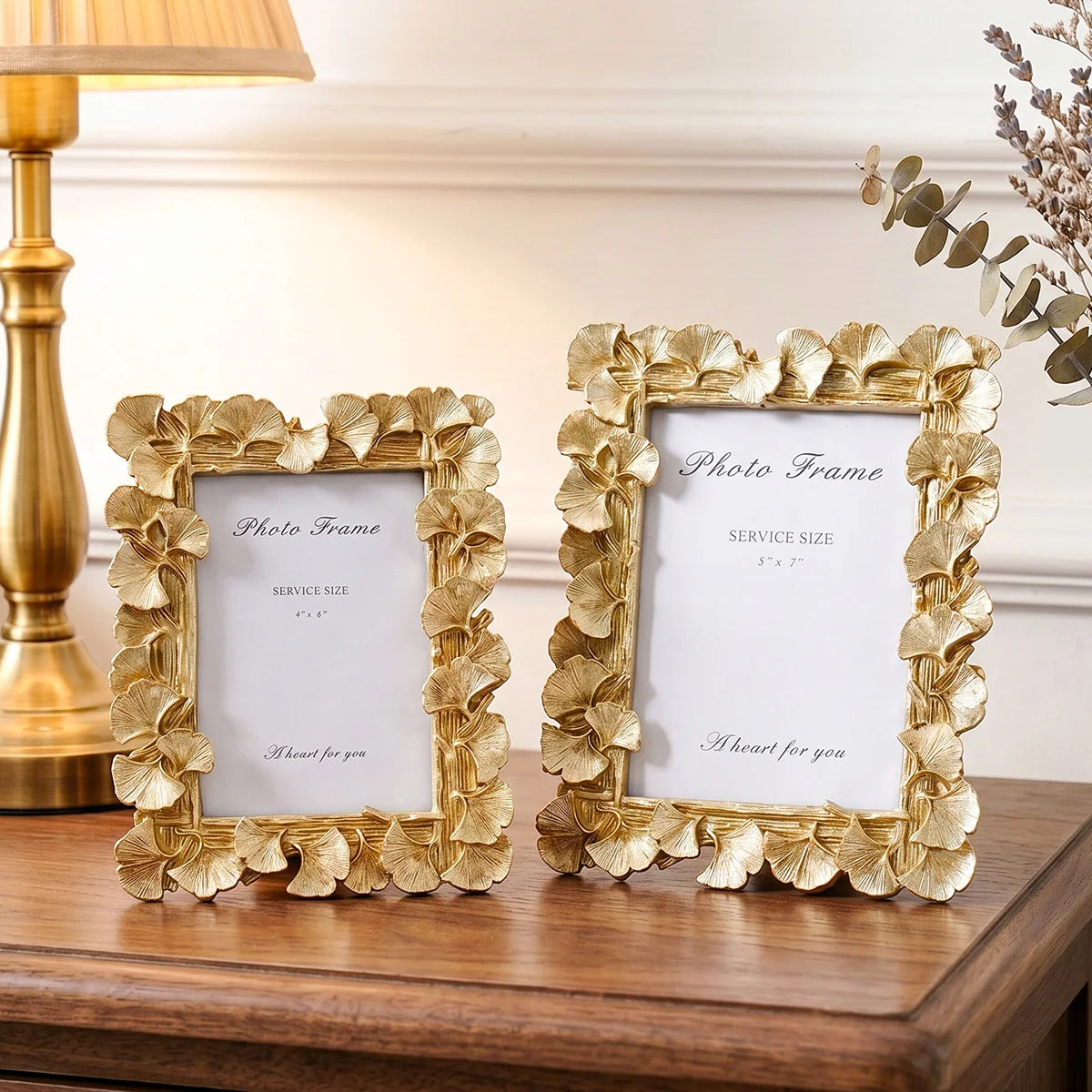 Two gold-framed photo frames with white mats and ginkgo leaf accents resting on a wooden surface.