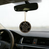 A round leather tag with gold lettering hangs from a rearview mirror on a car windshield.