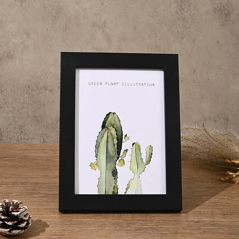 A black photo frame displaying a green plant illustration of a cactus on a wooden surface.