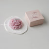 A pink rose-shaped scented candle in a square box is displayed on a white plate.
