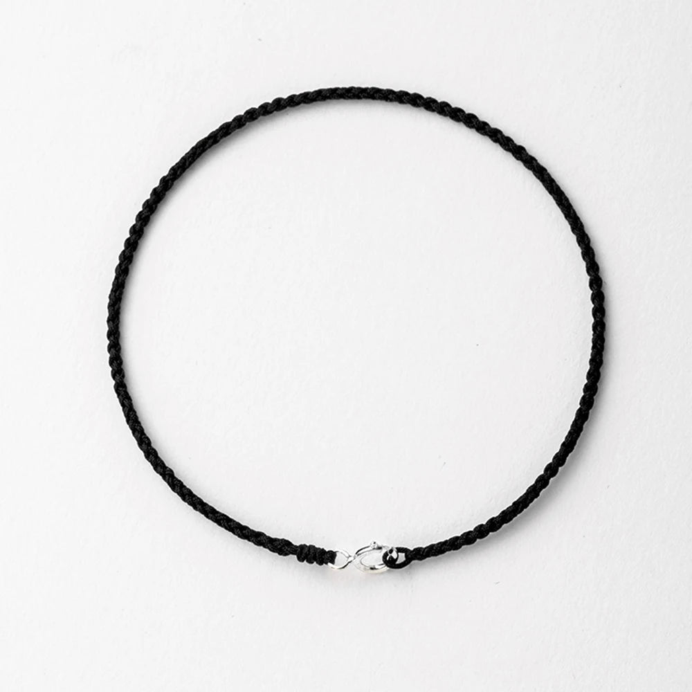 A black string bracelet with a gold plated clasp laid flat on a white background.