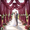 A wedding ceremony setup featuring a deep burgundy tulle draped backdrop and aisle decorated with pink and white flowers.