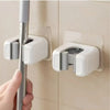 A hand is holding a silver mop holder attached to a white adhesive wall bracket.