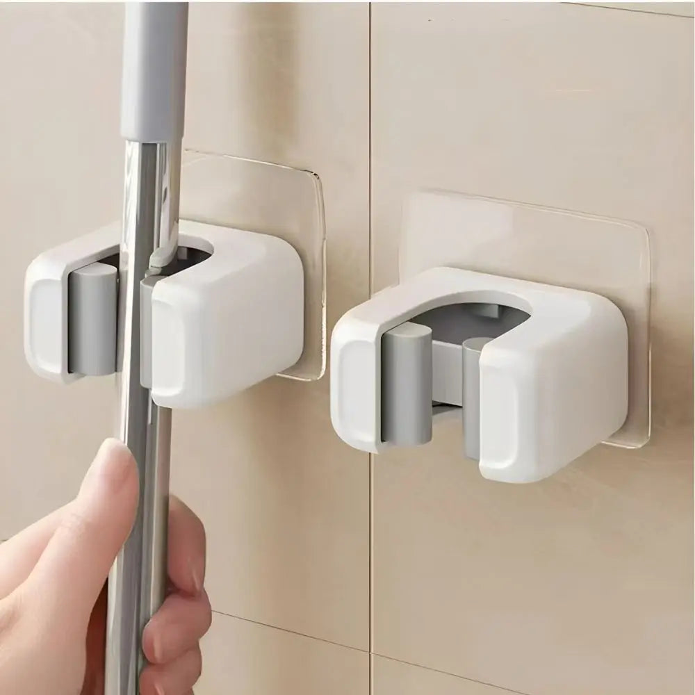 A hand is holding a silver mop holder attached to a white adhesive wall bracket.