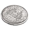 A detailed silver coin featuring a depiction of a meditating Buddha surrounded by foliage and decorative borders.