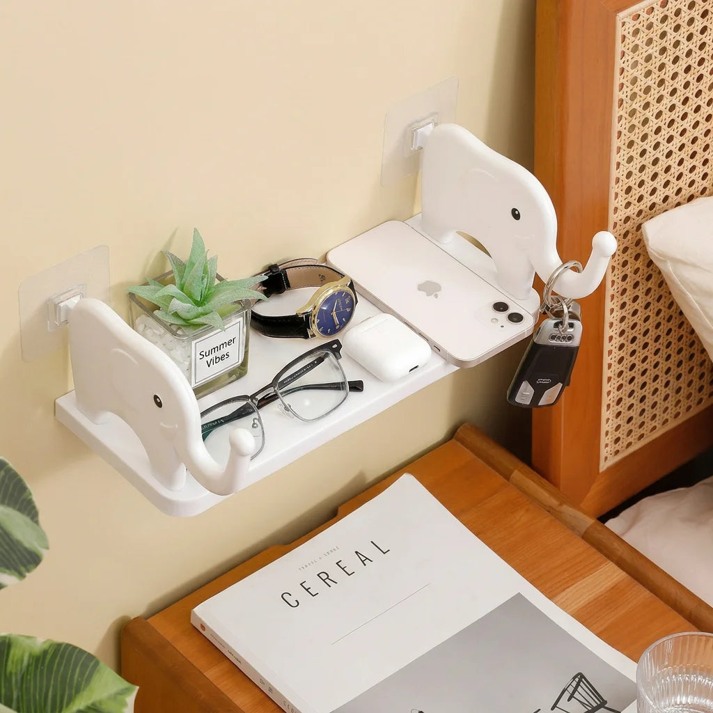A white adhesive elephant storage rack mounted on a wall, holding various items like glasses and a smartphone.