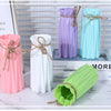 Three plastic vases in pink, purple, and light blue with rope accents displayed on a white marble surface.