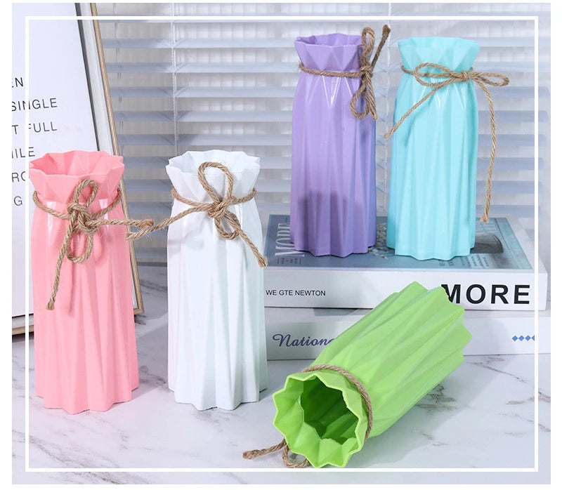 Three plastic vases in pink, purple, and light blue with rope accents displayed on a white marble surface.