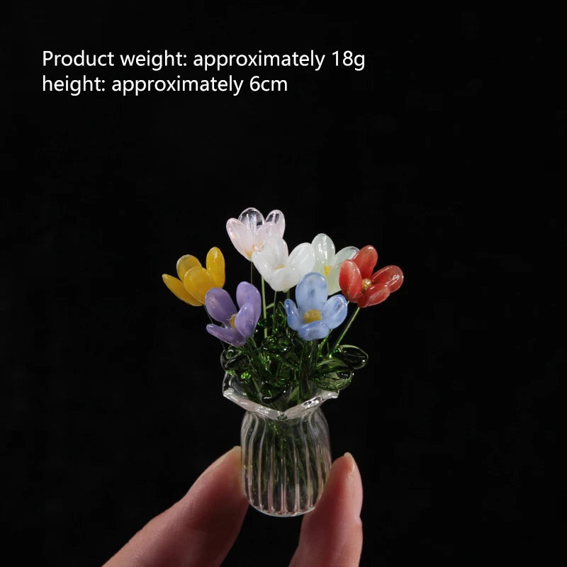 A hand holds a small glass vase filled with colorful handmade glass flowers.