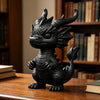 A black 3D printed mini dragon statue collectible sitting on a wooden desk next to books.