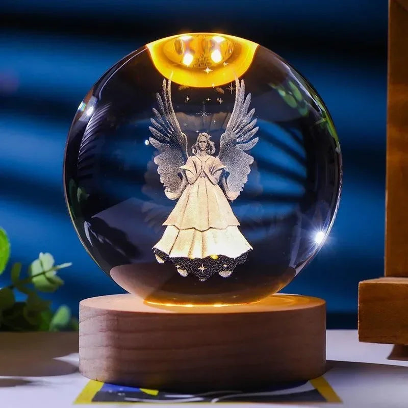A round glass crystal ball night light with a glowing yellow light featuring a silhouette of an angel's wings and figure.