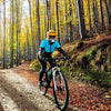 Une personne portant un casque et un masque jaunes fait du vélo sur un sentier de terre dans une forêt d'automne.
