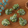 Collection de petites figurines de grenouilles de jade vertes posées sur une surface en bois.