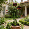 A decorative metal carnivorous flower garden stake with three vibrant, dark red and green flower heads growing in a terracott