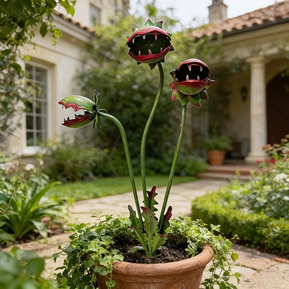A decorative metal carnivorous flower garden stake with three vibrant, dark red and green flower heads growing in a terracott