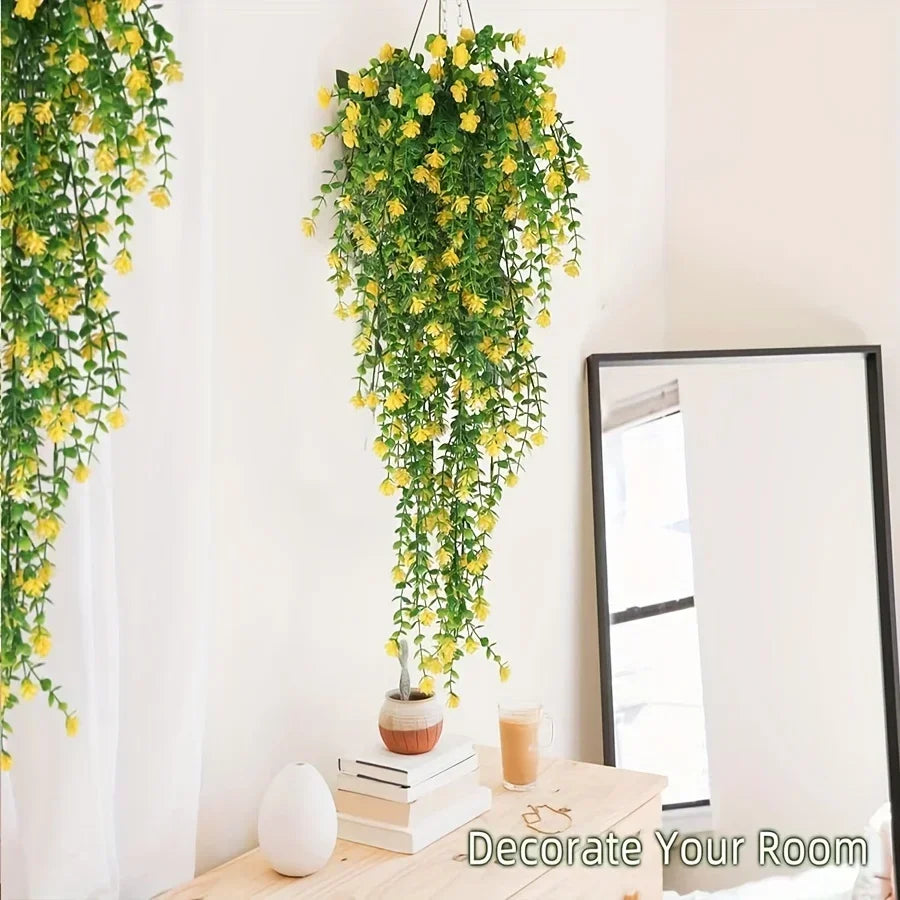 A vertical display of three lifelike faux eucalyptus hanging plants with yellow flowers against a white wall.