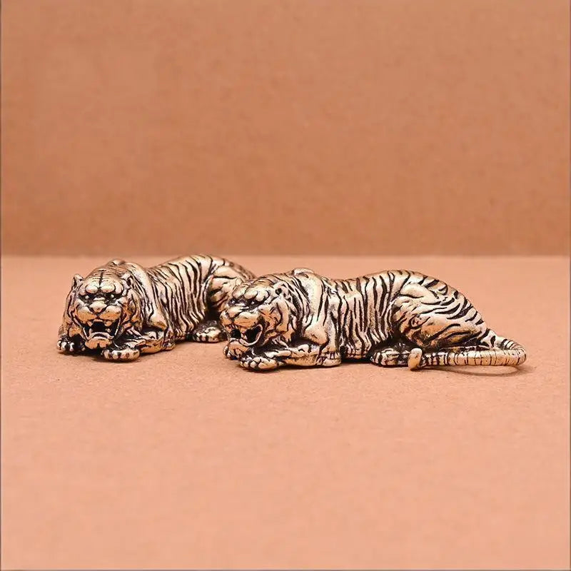 A pair of vintage brass tiger figurines in a striped pattern lying side by side on a neutral background.