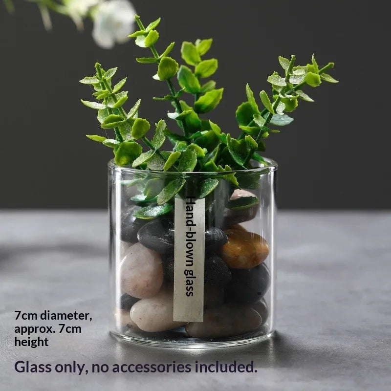 A clear glass vase filled with various sized dark and light stones used as decor for plants.