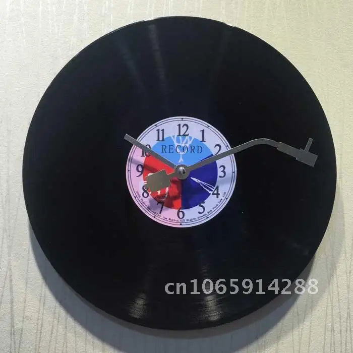 A black vinyl record wall clock with a white face and a blue and red center design.
