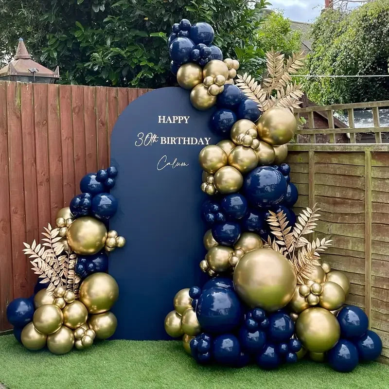 A balloon garland arch featuring navy blue and gold metallic balloons set against a dark blue backdrop.