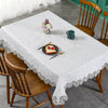 A white embroidered lace tablecloth is set on a wooden table with a floral centerpiece and food items.