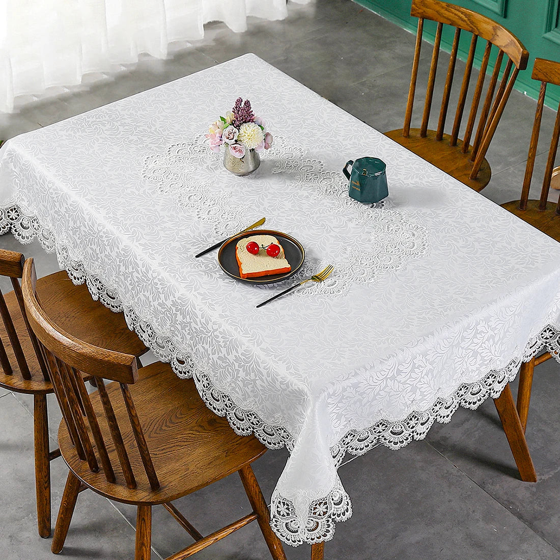 A white embroidered lace tablecloth is set on a wooden table with a floral centerpiece and food items.