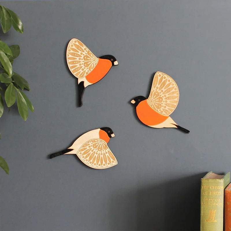 A set of three vintage wooden bird wall decorations in orange and black designs mounted on a gray wall.