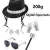A black sequin disco hat, tie, and glove set with a silver-colored accessory shown next to sunglasses.