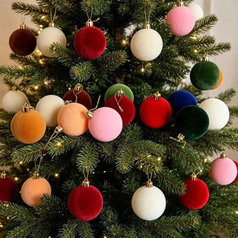 A close-up of a Christmas tree decorated with five velvet flocked ornaments in shades of pink, red, green, and white.