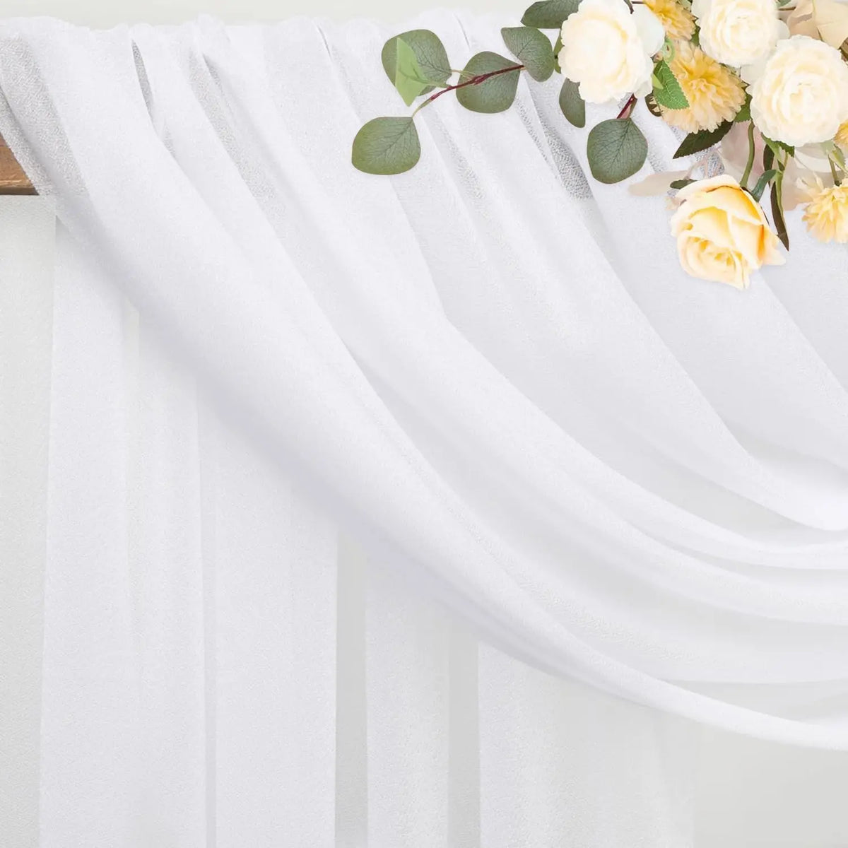 White sheer tulle draping fabric with green leaves and yellow roses used as a wedding arch backdrop.
