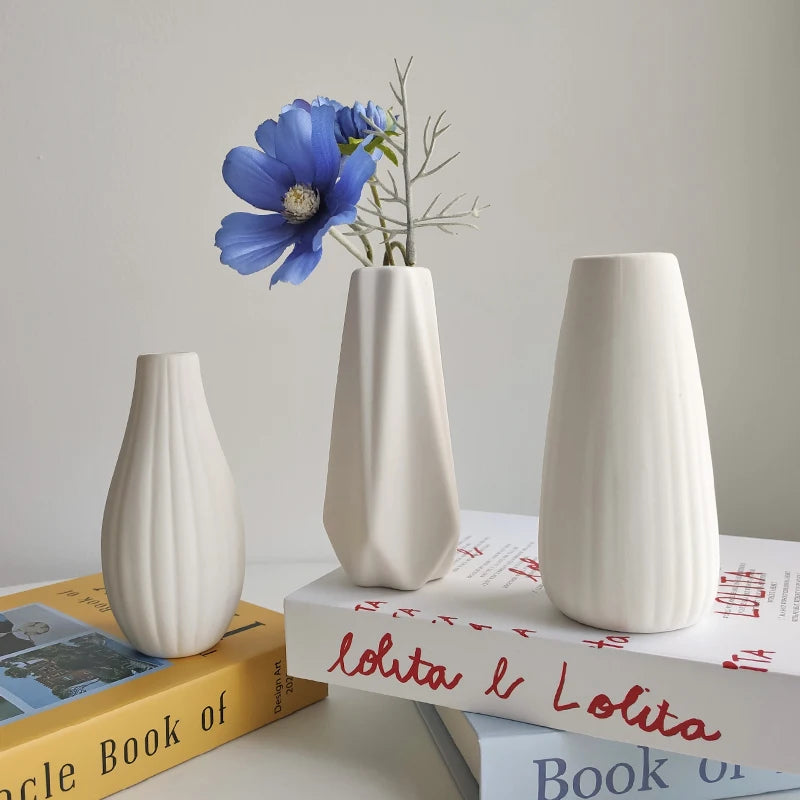 A white ceramic bud vase with vertical ridges holding a blue flower, displayed on a stack of books.