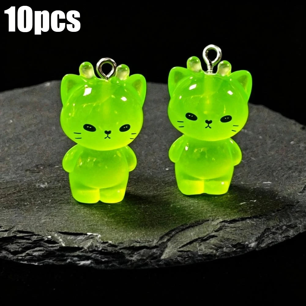 Ten pairs of glow-in-the-dark green cartoon kitty duck resin charms displayed on a dark surface.