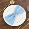 A set of ten light blue fringed cotton napkins placed on a white plate with gold rim and gold cutlery.