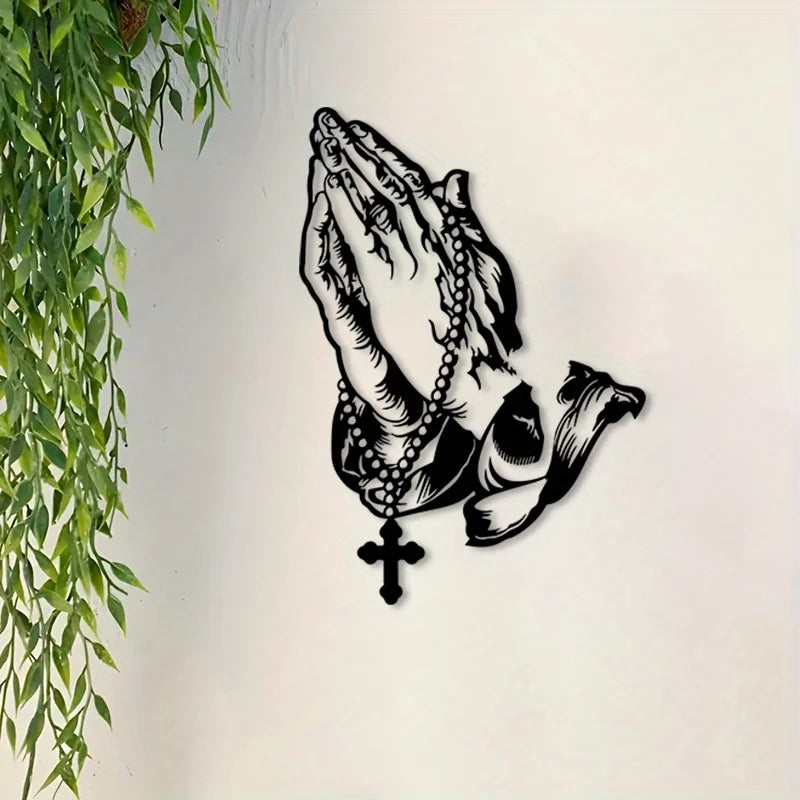 Black metal wall art depicting praying hands with a cross design.