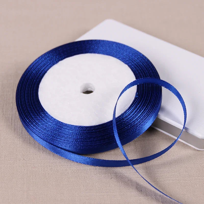 A spool of royal blue satin ribbon with a white center core resting on a white rectangular surface.
