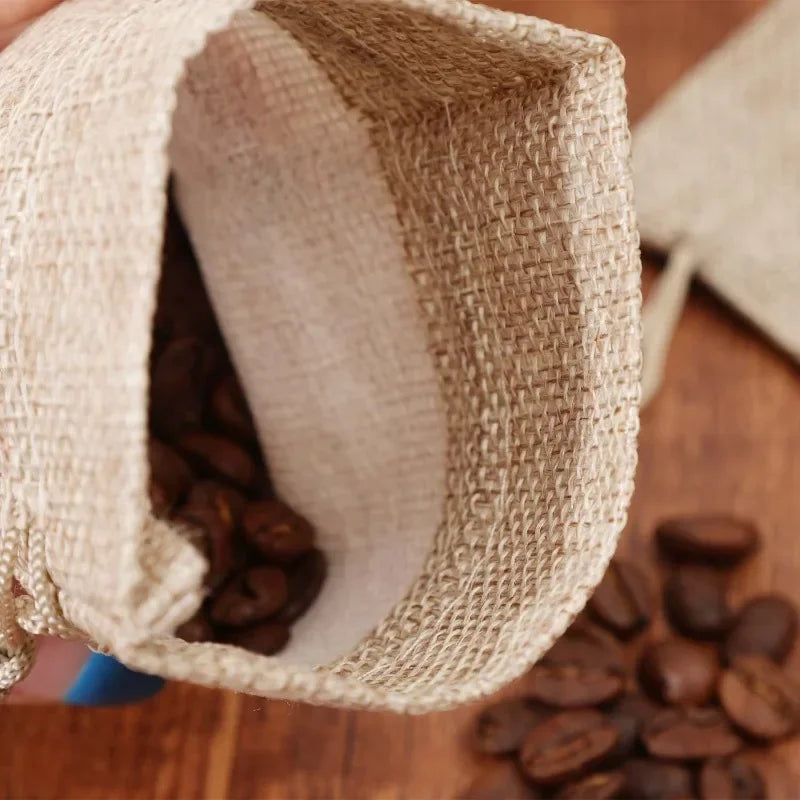 A close-up view of a natural burlap drawstring bag partially open, showing dark roasted coffee beans inside.